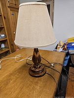 Full view of the lamp showing the beige fabric shade and inlay wood base and body, placed on a wood surface.