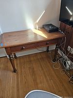 Full view of antique pine wood desk with two drawers and turned legs, placed against a wall with electronic device on top and cables underneath.