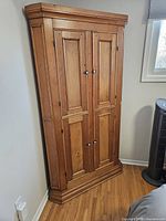 Full view of pine corner cabinet in room corner showing front elevation.