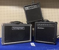 Three guitar amplifiers displayed: a Traynor TS-10, a Silvertone, and a smaller unbranded black amplifier, all visible from the front showing brand logos and speaker grills.