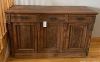 Front view of the antique wooden sideboard showing three drawer fronts and three door panels with carved details and metal hardware.