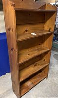 Front angled view of wooden bookcase showing five shelves and natural wood grain.