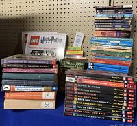 Full view of stacks of boys books on a blue cloth with pegboard background, showing diverse titles including Hardy Boys, Bone graphic novels, A Series of Unfortunate Events, and others.