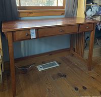 Front view of the wooden computer desk showing two small drawers and a smooth wooden top with some wear.