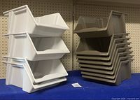 Stacked heavy duty plastic stacking bins, showing 4 white bins and 8 brown bins stacked separately on a blue surface in front of a pegboard.