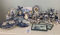 Large lot of assorted blue and white Dutch-themed ceramics and collectibles arranged on a shelf, featuring plates, figurines, vases, a decorative clock, and small decorative items.