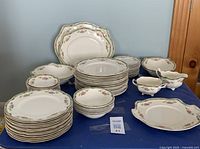Full lot view showing multiple stacks of plates, bowls, serving pieces, including platters, cups, and a gravy boat, all with a floral rim pattern and green and gold trim.