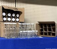 Full lot view showing 32 clear plastic bottles arranged in front of cardboard partitions and boxes, including larger 355 ml and smaller 60 ml bottles with white caps.
