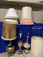 Three vintage table lamps displayed on blue cloth with an array of lampshades and frames, showing varied condition and fabric damage on shades.