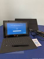 Tablet with keyboard attached, screen showing setup prompt, pen on keyboard, pouch and charger in background