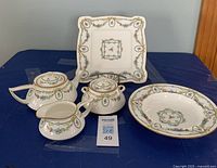 Full view of Minton tea service items including teapot, creamer, sugar bowl with lid, sweets plate, and shallow bowl arranged on blue cloth.