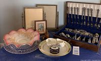 Photo showing the assembled lot: silverware set in wooden case, decorative pink and gold glass bowl on clear glass plate, porcelain plate, teacup and saucer, Limoges pill box, small framed artwork, two standing photo frames