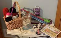Full lot setup showing basket with yarn skeins, knitting looms, pattern booklets, and various knitting accessories on table.