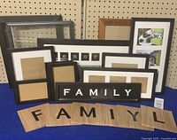 Array of multiple picture frames in different sizes and styles on a blue surface with a pegboard background. Includes two 'Family' themed decorative pieces.