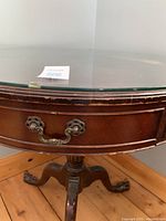 Close-up of table drawer with ornate metal handle and edge of tempered glass top showing wear and scratches on wood surface.