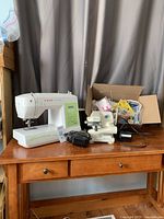 Photo of Singer Sew Mate sewing machine, Baby Lock blind hemmer sewing machine, and a box of sewing notions on wooden table with curtain background