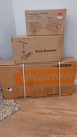 Three boxed children's ride-on items stacked: Fealarfaith Mini Bike box on top, Kick Scooter box in middle, Chipmunk bicycle box on bottom.