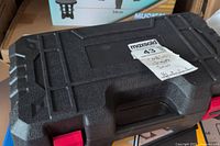 Closed black plastic carrying case with red latches, labeled 'cordless saw'