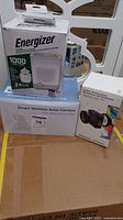 Boxed Energizer 1000 lumen lantern power bank, smart wireless solar camera, and Saramonic wireless microphone boxes on cardboard surface.