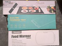 Photo showing the three boxed items: Flexible electric warming mat by YONZO, Electric warming tray, and Thoahhe Food Warmer, arranged stacked together.