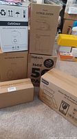 Photo of boxed kitchenware items including CalfeGrace milk frother, citrus juicer, ice shaver machine, Bay22 glass containers, and other boxes on carpeted floor.