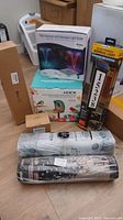Photo showing all items including pool fountain box with LED hexagon light show, Sensor Brite solar address light box, HIXX smart bird feeder box, solar deck lights box, and two rolled kitchen or entry rugs.