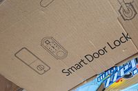 Close-up of smart door lock box showing a printed image depicting the handle, keypad, and deadbolt components with wording 'Smart Door Lock'