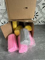 Open cardboard boxes showing individually wrapped super absorbent cleaning sponges in pink, yellow, and gray.