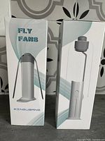 Two boxed fly repellent fans, white, with flexible neck and switch, shown in their retail packaging.