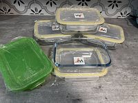Set of 4 glass storage dishes stacked with their 4 matching plastic lids, and one green plastic lid placed beside them.