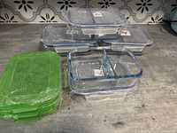 Photo showing stacked clear rectangular glass casserole dishes with dividers and two different sets of lids, blue locking lids on top, and green flexible lids on the side.