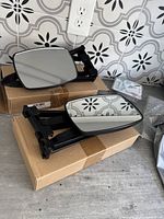 Two adjustable towing mirrors resting on cardboard boxes with tiled backsplash in background