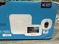 Damaged blue retail box showing model AC327 and images of the baby monitor set components.