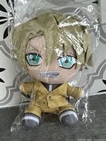 Plush doll sealed in original plastic packaging laid on patterned surface showing character with light brown hair, teal eyes and yellow suit.
