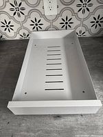 Top view of white metal shelf slider showing vented base and clean finish on countertop with patterned tile backdrop.