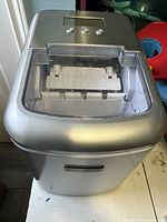 Front view of the silver Kumio ice maker with transparent lid showing the ice tray inside.