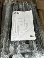 Photo of the unassembled black metal parts and wood base wrapped in plastic along with the instruction manual showing the rack design and model number 03LB01.