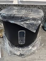 New Amazon Basics paper shredder partially wrapped in clear plastic with large black waste bucket below on floor.