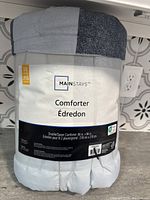 Photo of comforter in original packaging with label showing brand Mainstays and size 86 x 86 inches, double/queen comforter.