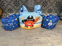 Front view of a blue water wing swimming vest for toddlers showing colorful printed designs and crab cartoon on chest.