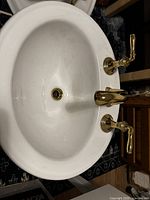 Top view of one white oval KOHLER sink showing gold-tone widespread faucet with two handles, drain hole without cover.