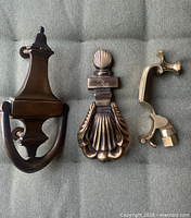 Three antique brass door knockers laid flat on fabric background showing varying sizes and designs.