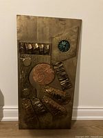 Front view of bronze abstract wall sculpture with geometric and organic embossed shapes including a turquoise circular element and copper floral motif.