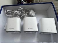 Photo showing three white D-Link mesh Wi-Fi units with power cables inside a blue box.