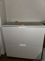 Front view of white metal drawer unit showing two drawers with integrated handles and lock on top drawer