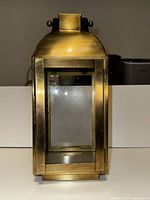 Front view showing polished golden brass rectangular candle holder with glass panels and decorative side knobs.