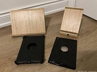 Two wooden iPad stands positioned upright and two black protective iPad cases laid flat on floor, showing rotating circle cutouts.