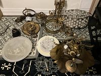 Overall view of seven assorted antique and modern electrical light fixtures on patterned carpet, showing varied brass, glass, and crystal components laid out for inspection.