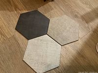 Three hexagonal tiles in black, white-grey, and grey on wood floor showing shape and texture.
