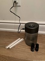 Lexon aroma diffuser plugged in with power cord, placed on hardwood floor with three white incense sticks and two small essential oil bottles beside it.